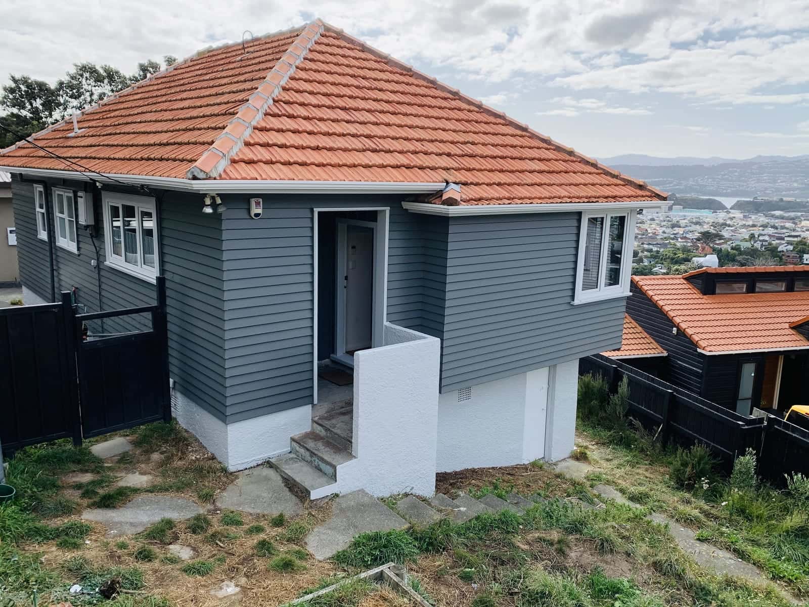 A charcoal-grey weatherboard house with white trims and a terracotta tile roof